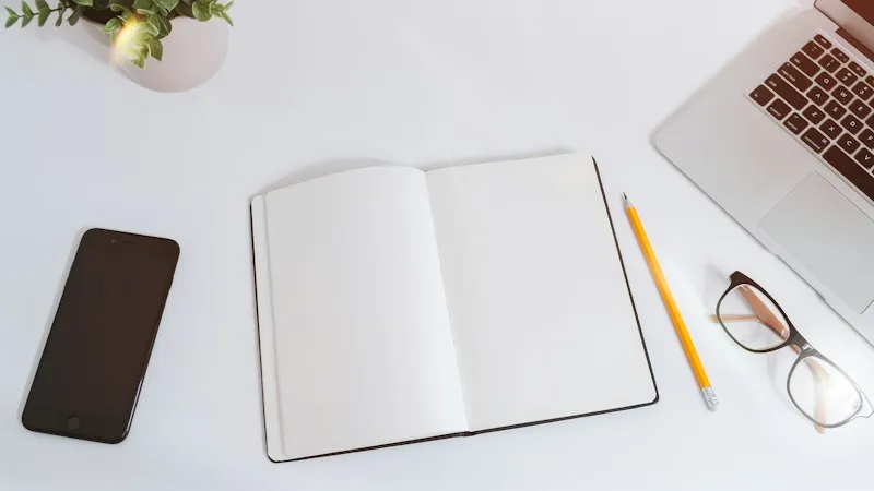 An open notebook beside a phone and laptop on a white desk